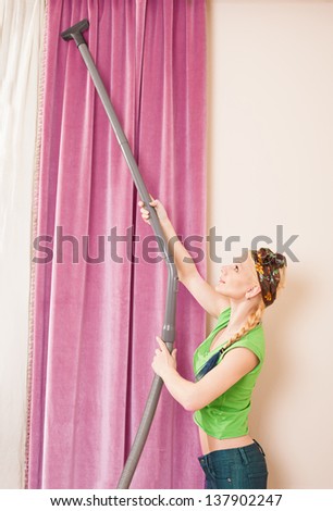 beautiful young lady using a vacuum cleaner for hoovering the curtains