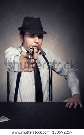 retro gangster with a gun wants you dead on grunge background.shallow depth of field with the gun in focus