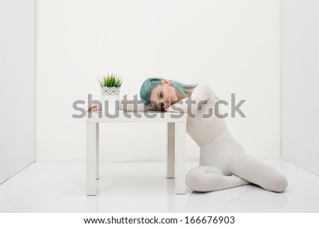 young sad lady in a white room with a small table and a plant