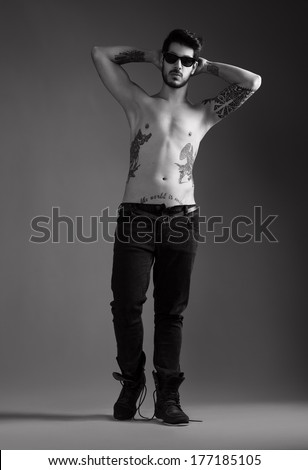 handsome young man with several tattoos posing topless for camera