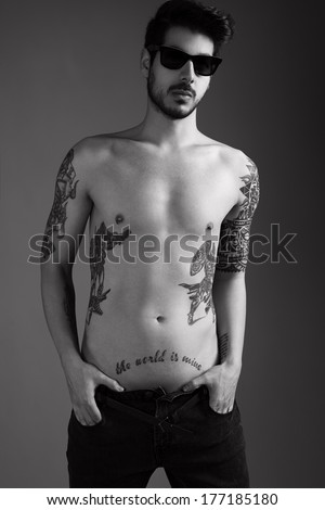 handsome young man with several tattoos posing topless for camera