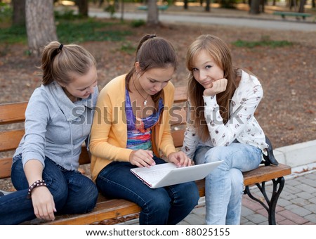Portrait of three pretty student girls in the park and surfing the internet