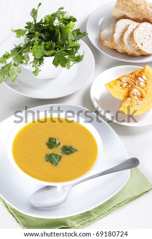 Pumpkin soup in a bowl, two pieces of pumpkin, parsley and bread