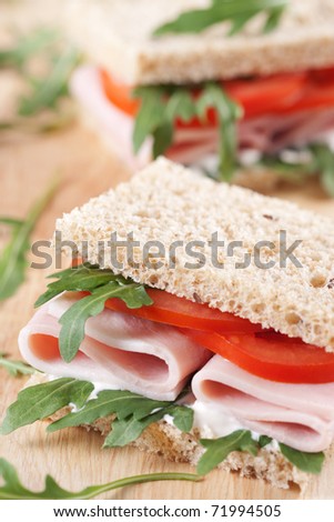 Sandwich with ham,tomato, and rucola salad on the wooden cutting board