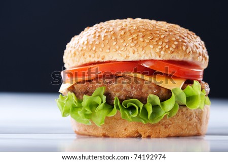 Cheeseburger with tomatoes and lettuce on black background