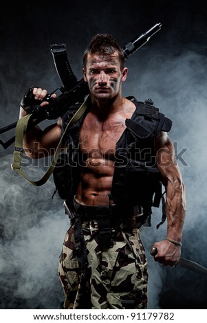 Muscular young sexy naked soldiers with knives and weapons in army clothes and flak jacket in the smoke