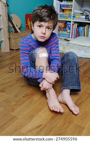 Young boy with band aid on his knee is holding his leg