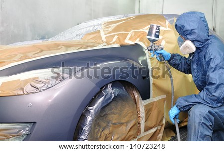 Worker painting car in a paint booth.