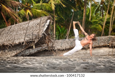 Yoga vasisthasana side plank pose by fit man in white trousers on the beach near the fishermen boats in Varkala, Kerala, India