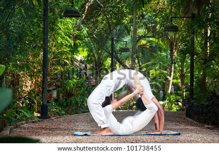 Couple Yoga of man doing chakrasana and woman doing dhanurasana poses in white cloth in the garden. Represents yin and yang
