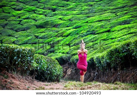 Yoga garudasana eagle pose by woman in red cloth on tea plantations in Munnar hills, Kerala, India