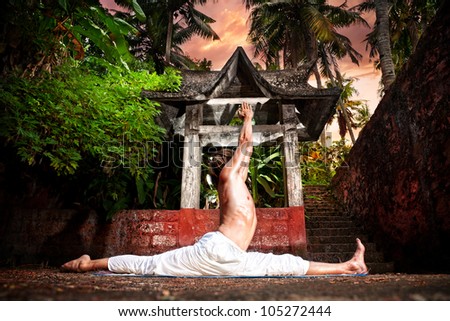 Yoga hanumanasana monkey pose by man in white trousers near stone temple in tropical forest