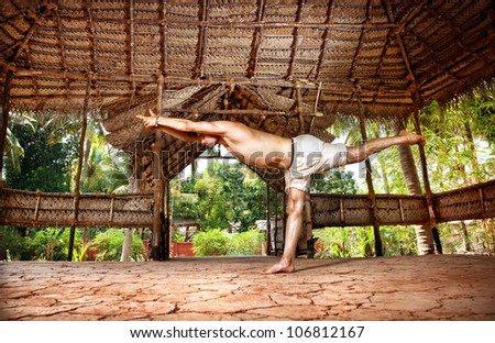 Yoga virabhadrasana III warrior pose by fit man in white trousers on the drought earth in yoga shala, Varkala, Kerala, India