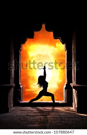Yoga virabhadrasana I warrior pose by woman silhouette in old temple arch at dramatic sunset sky background. Free space for text