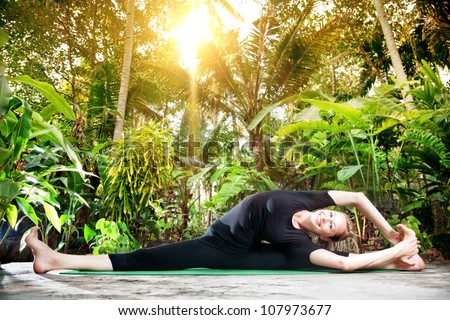 Yoga parivrtta janu sirsasana pose by smiling woman in black cloth in the garden with palms and banana trees