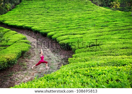 Yoga virabhadrasana I warrior pose by woman in red cloth on tea plantations in Munnar hills, Kerala, India