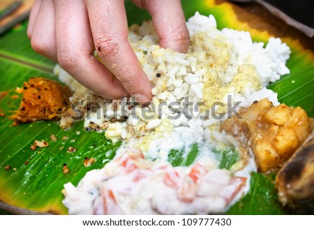 Man eating Indian traditional vegetarian thali from rice, dal, potatoes, tomato salad on banana leaf in restaurant