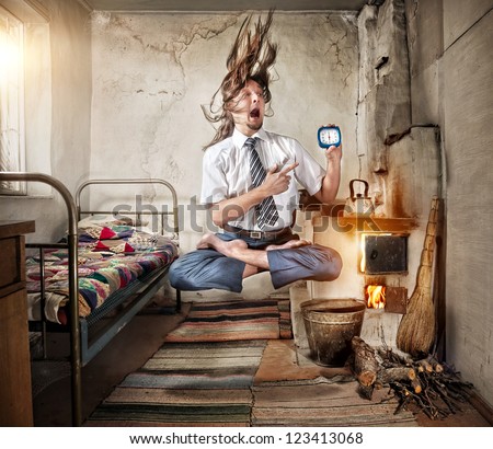 Stressful Businessman levitating in yoga lotus pose with alarm clock in his hand in old Russian house with traditional stove