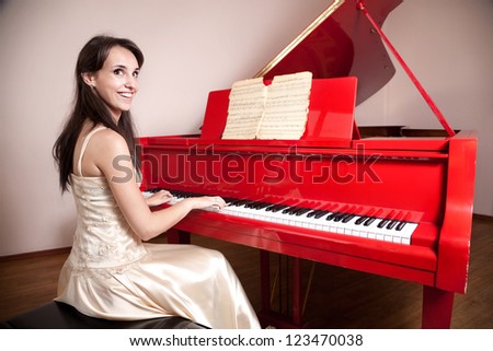 Happy woman in dress playing the red grand piano, smiling and looking at camera
