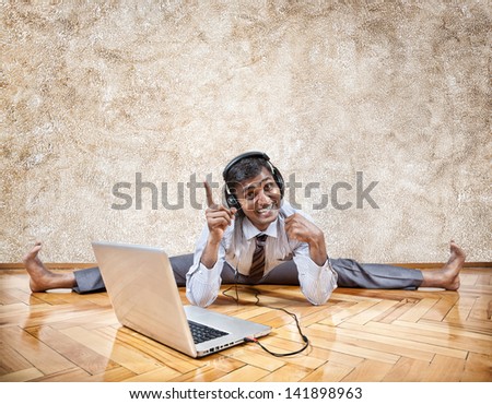 Indian businessman listening to the music with headphones and doing yoga near the laptop in the office