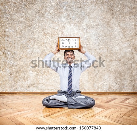 Happy Indian businessman holding big clock in meditation pose in the office