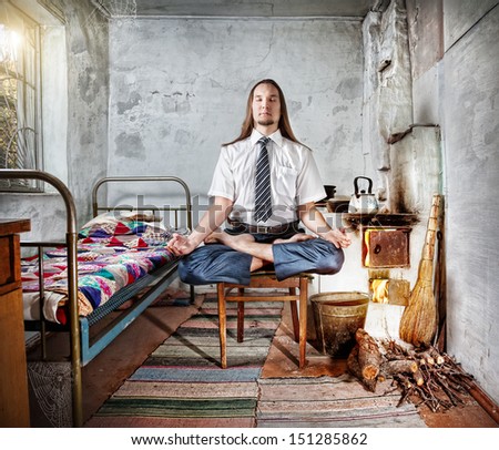 Businessman with long hair doing meditation in old Russian house with traditional stove