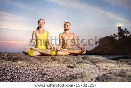 Couple doing meditation in lotus pose on the stone near the sea at lighthouse background in Kovalam, Kerala, India