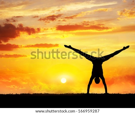 Man doing Yoga handstand on the grass at sunset sky
