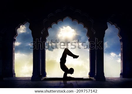 Man silhouette doing yoga advance scorpion pose in old temple at sunset sky background