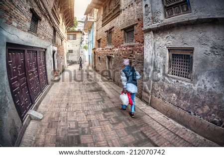 PATAN, KATHMANDU VALLEY, NEPAL - APRIL 28, 2014: Old man walking down the street in the Nepalese traditional hat near Patan Durbar Square