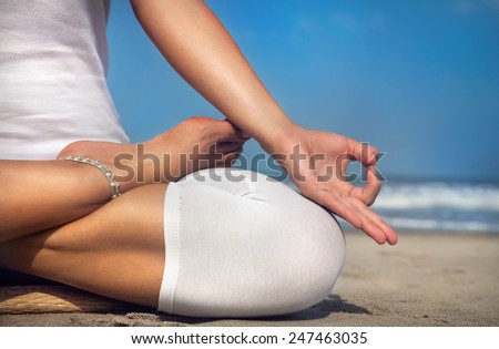 Woman doing yoga meditation in white costume on the beach in Goa, India