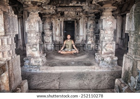 Man doing meditation in ancient temple with carving columns in Hampi, Karnataka, India
