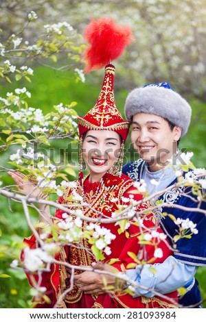Happy couple in Kazakh costumes in Spring Blooming apple garden of Almaty, Kazakhstan, Central Asia