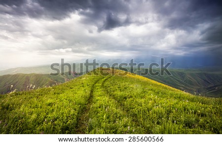 Grass Field with auto track and mountains at dramatic overcast sky in Ushkonyr near Chemolgan, Kazakhstan, central Asia