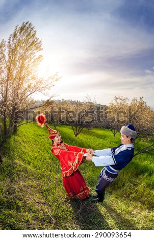 Kazakh woman in red dress dancing with man in Spring apple garden in Almaty, Kazakhstan, Central Asia