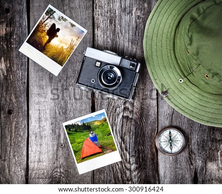 Old film camera, photos with tourist in nature, hat and compass on the wooden background