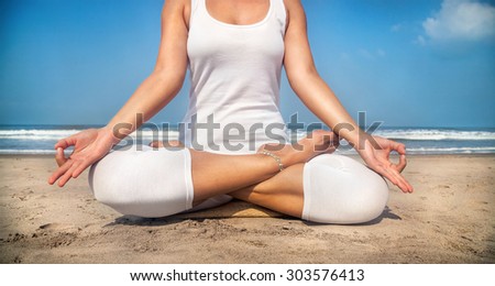 Woman doing yoga meditation in white costume on the beach in Goa, India