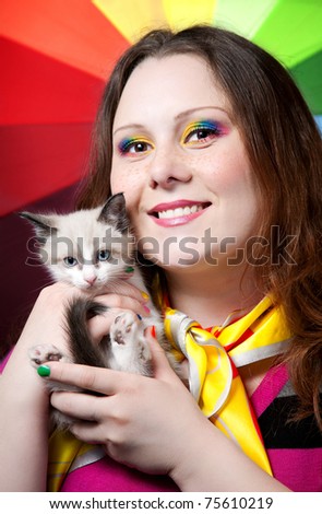 Beautiful woman with creative rainbow make-up and nails smiling and holding little kitten in her arms at rainbow background