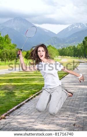 Furious Woman in sport cloth playing badminton and jumping with racket in park at mountain background