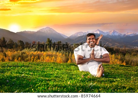 Yoga eka pada shirasana foot behind the head pose by happy Indian Man in white cloth in the morning at mountain and sunset sky background