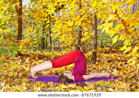 Yoga halasana plough pose by beautiful woman in red cloth and yellow leaves around in the autumn