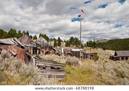 Tattered American flag and a Montana flag on a wooden flag pole fly over a section of this Montana ghost town
