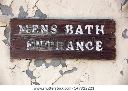Old weathered sign reading Mens Bath Entrance hanging on historic structure