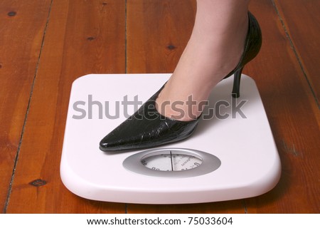 Stiletto foot on white bathroom scale on wood floor