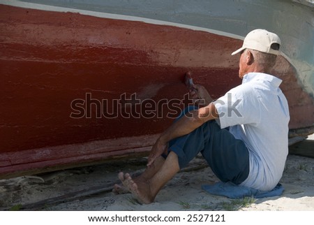 A man slowly painting the hull of an old boat.