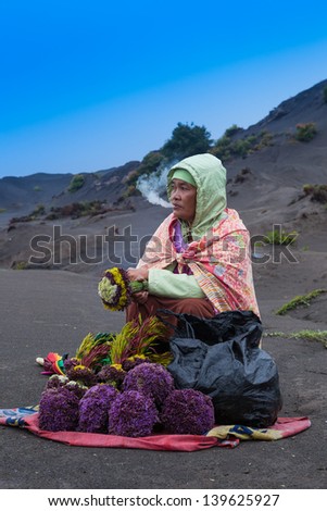 JAVA, INDONESIA - MARCH 2: woman smokes handmade  cigarette and sells bouquets flowers for sacrifice to Bromo volcano on March 2, 2013 in Java, Indonesia