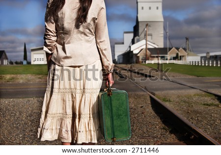 A stock image of a small town young woman holding an old suitcase and waiting for a train.
