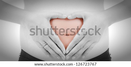 Young Woman Holding her hands in a heart shape on her pregnant belly. Black and White tone.