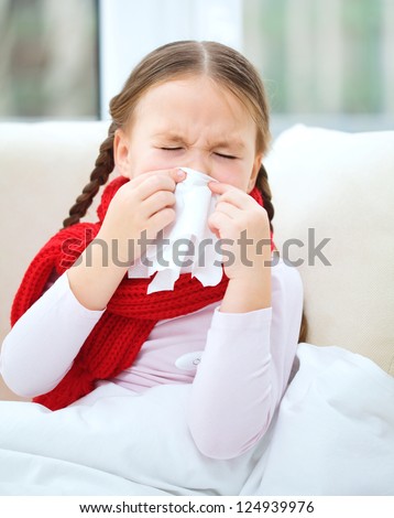Little girl is blowing her nose while sitting on a sofa