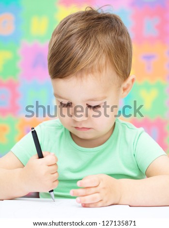 Little boy is writing on his copybook in preschool
